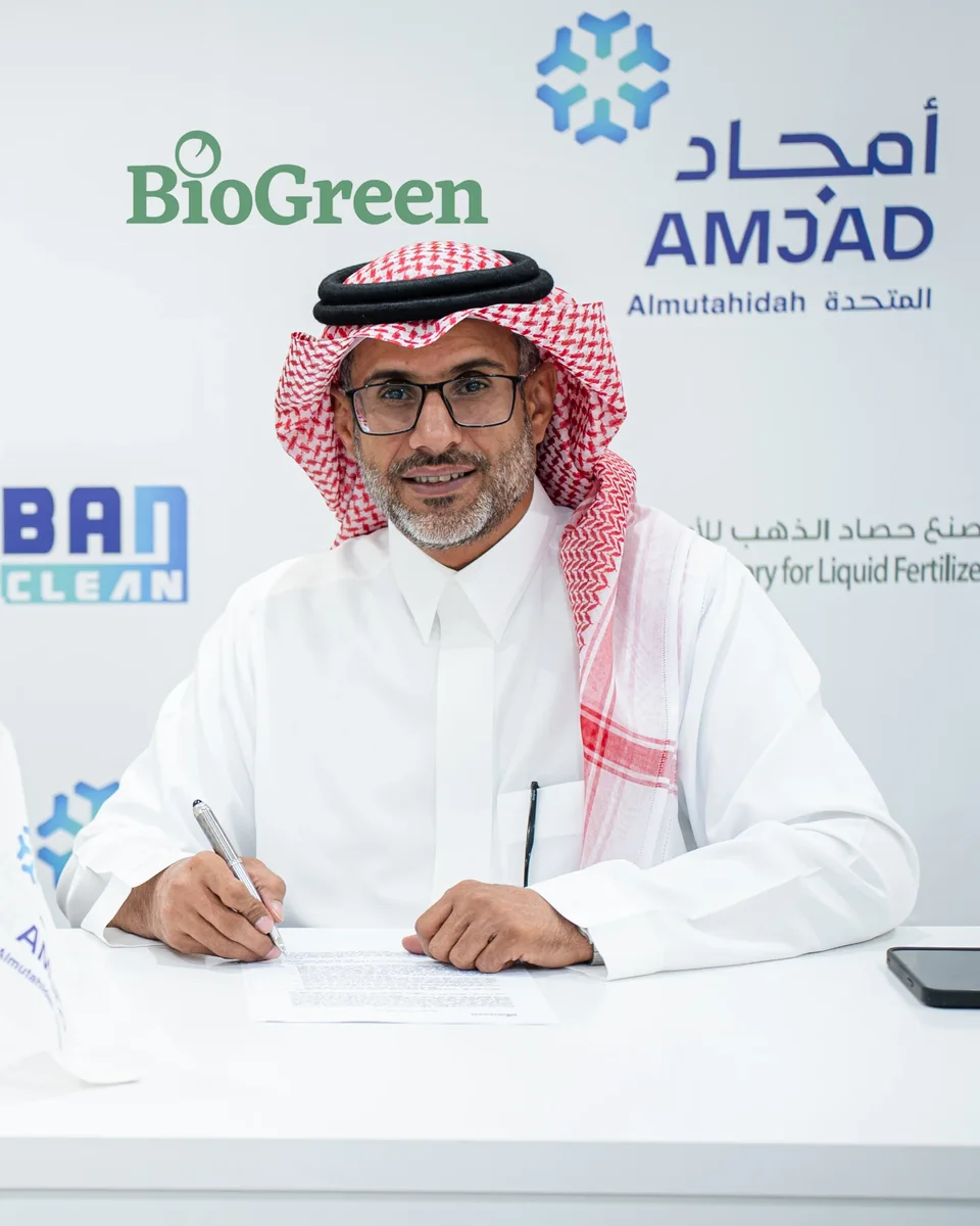 بندر محمد الغامدي، الرئيس التنفيذي لأمجاد المتحدة، يوقّع اتفاقية أمام شعارات علامات المجموعة